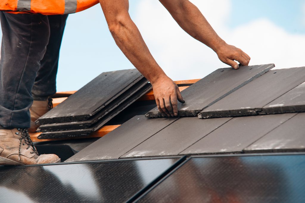 Roofer,Installing,New,Slate,Tiles,On,Residential,Roof,Under,Blue