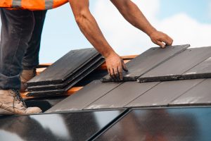 Roofer,Installing,New,Slate,Tiles,On,Residential,Roof,Under,Blue